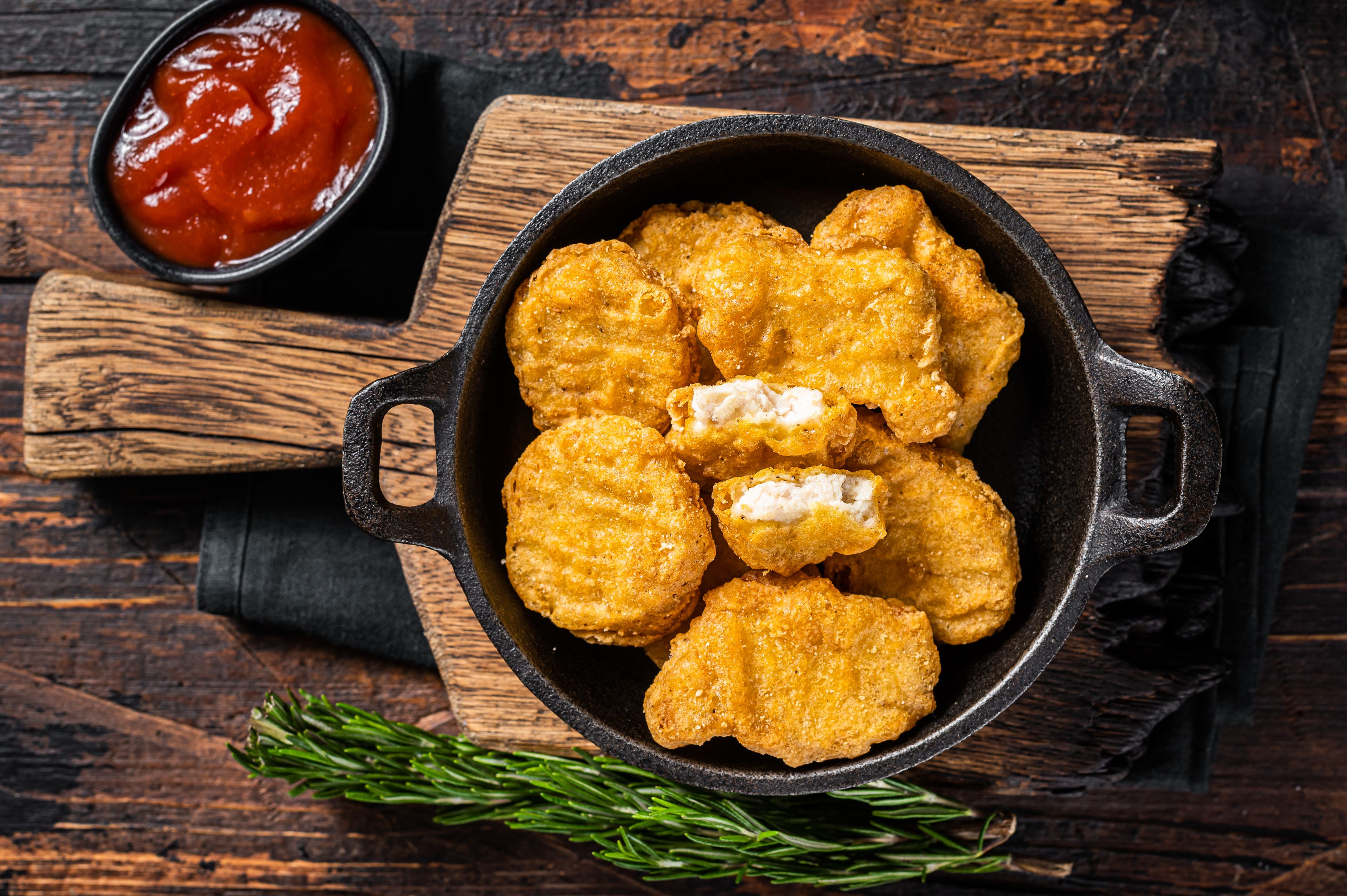 gebratenes Hähnchenschnitzel mit Zitronenscheiben, Kartoffelspalten und weißer Soße auf einem weißen Teller