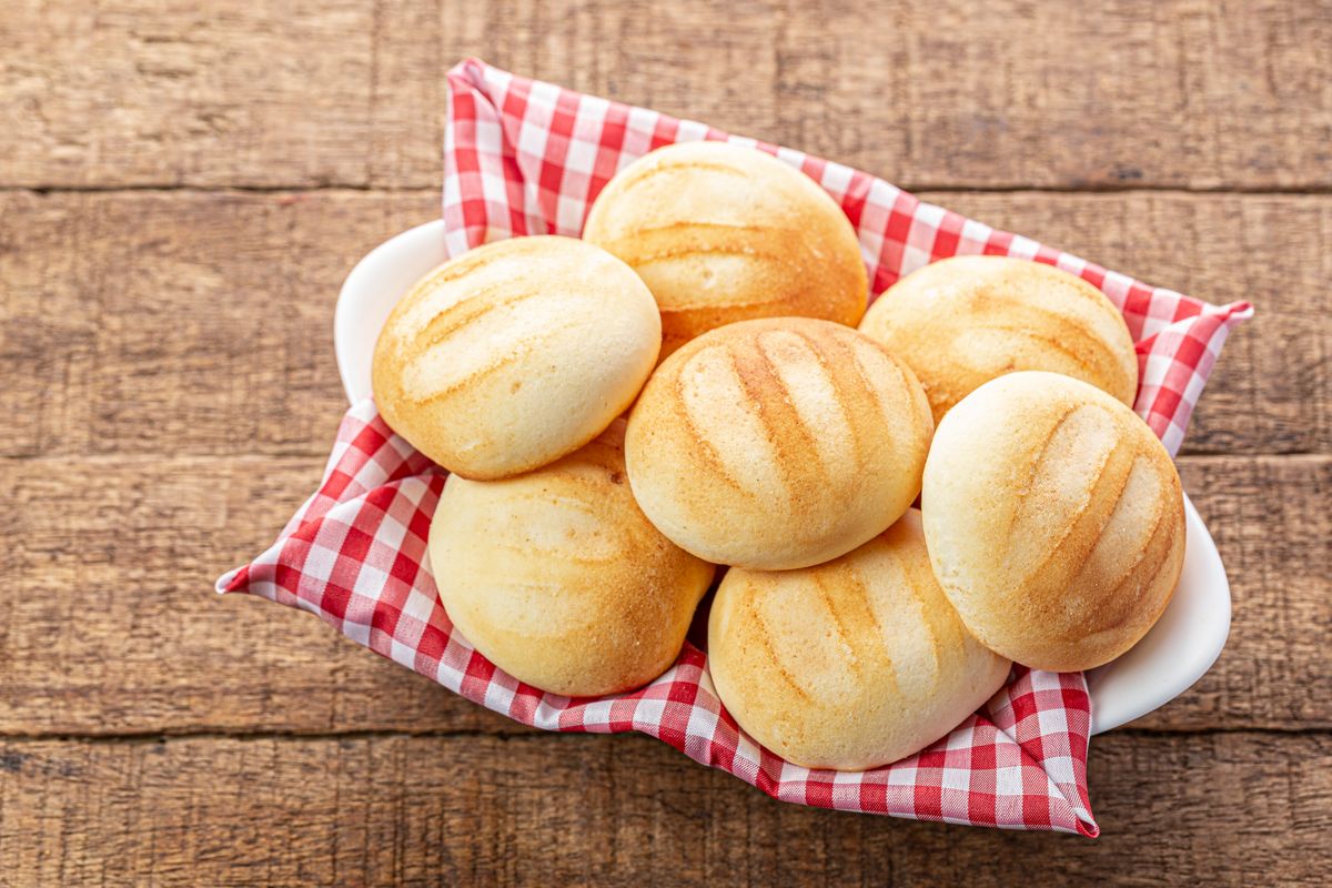 Aufbackbrötchen auf einem rot-weiß karierten Tuch in einer Schale auf einem rustikalen Holztisch
